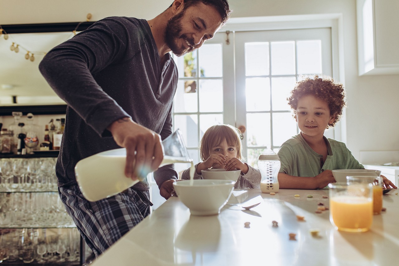 Man pouring milk in to bowls for breakfast at home. Father and kids having breakfast at home.