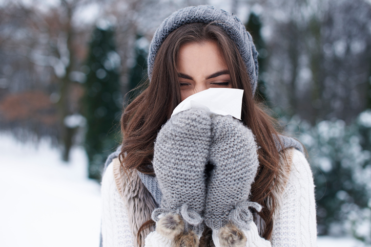 Eine Frau mittleren Alters, die sich draußen im Schnee die Nase putzt.
