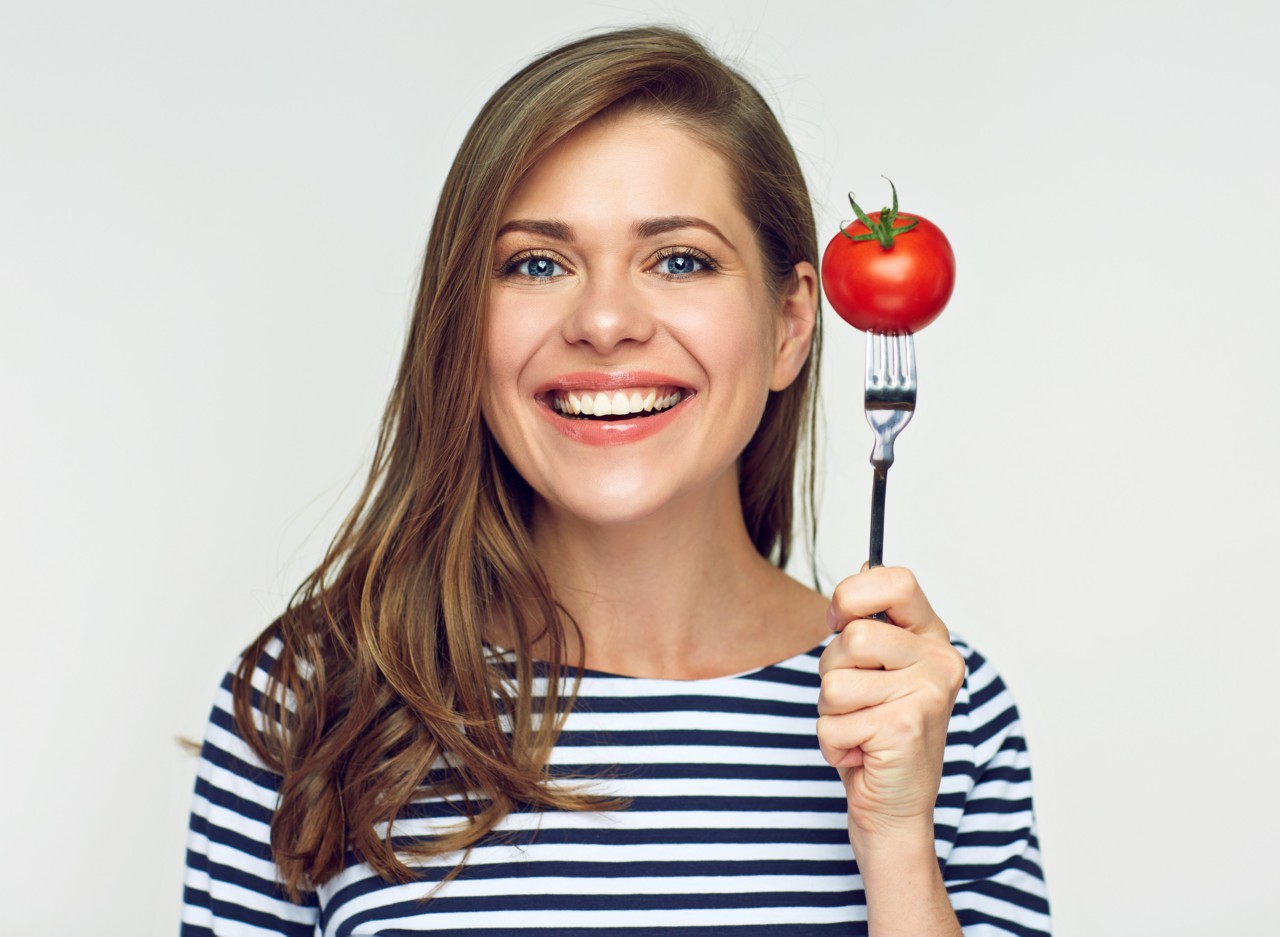 Smiling young woman holding tomato on fork. Isolated portrait with dieting concept.