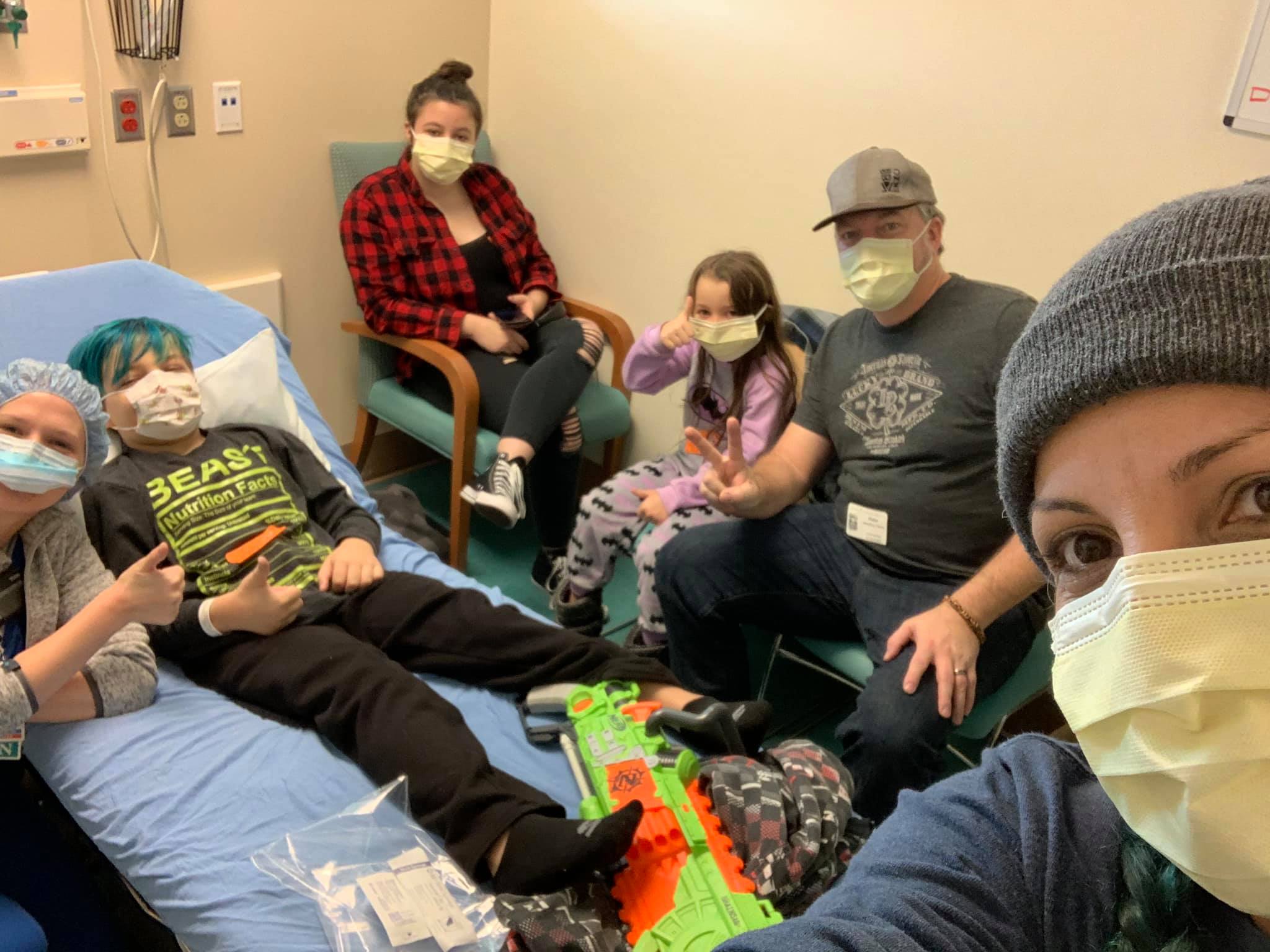 Gideon gives the thumbs up during a hospital visit while surrounded by his family.