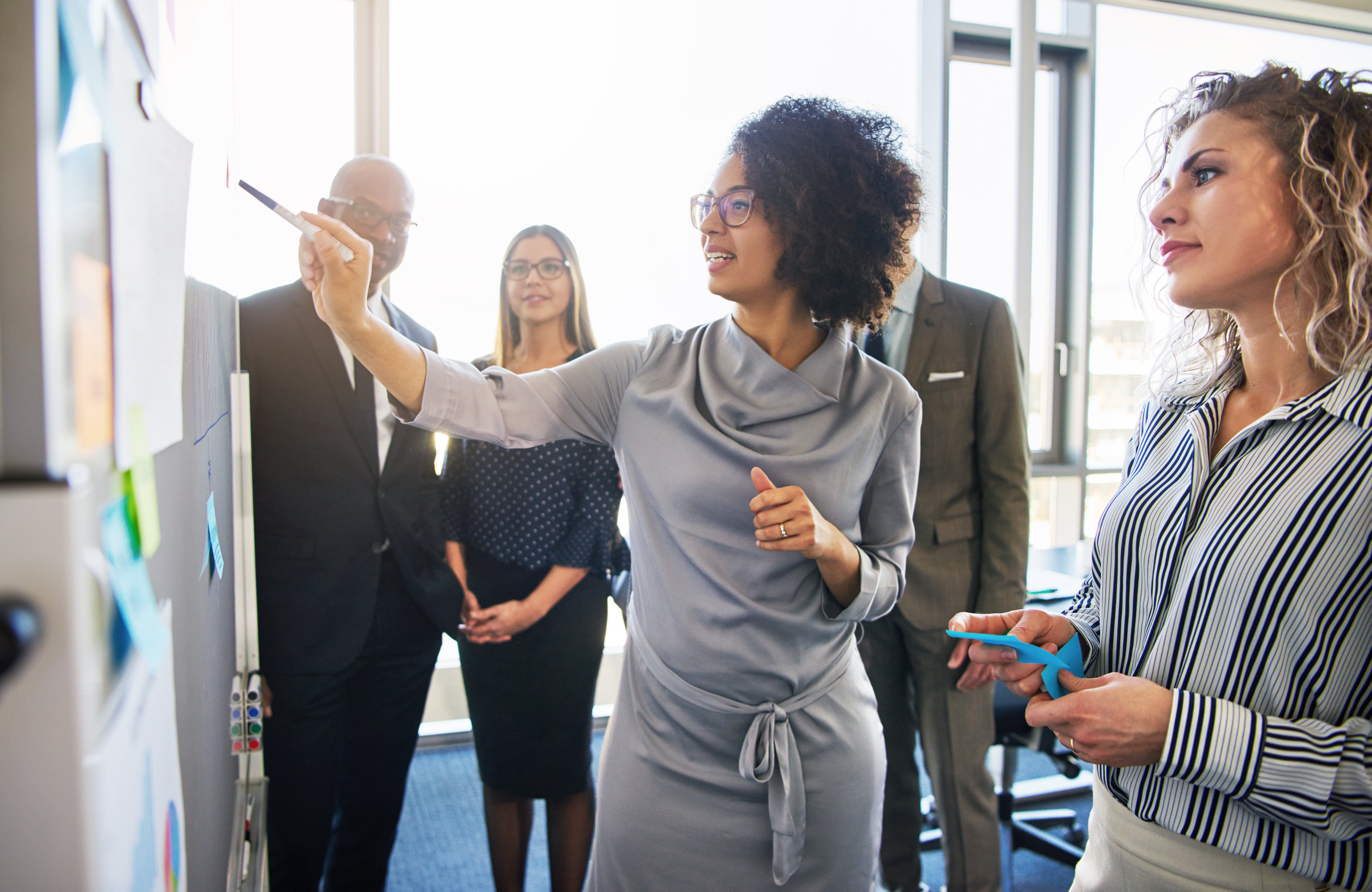Diverse group of focused businesspeople brainstorming together on a whiteboard during a strategy session in a bright modern office; Shutterstock ID 748719808; Purchase Order: Brand Newsletter